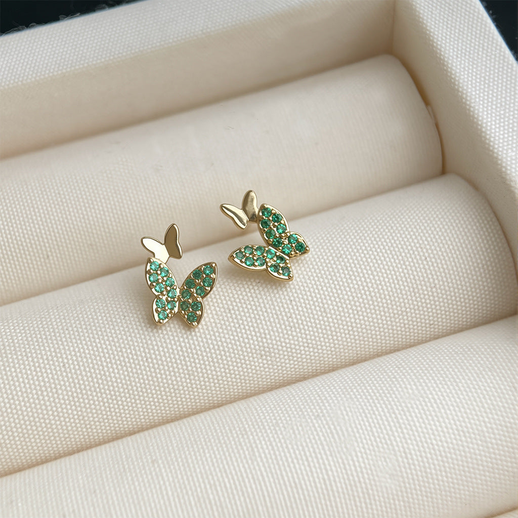 Butterfly-shaped earrings with green gemstones on a soft beige surface