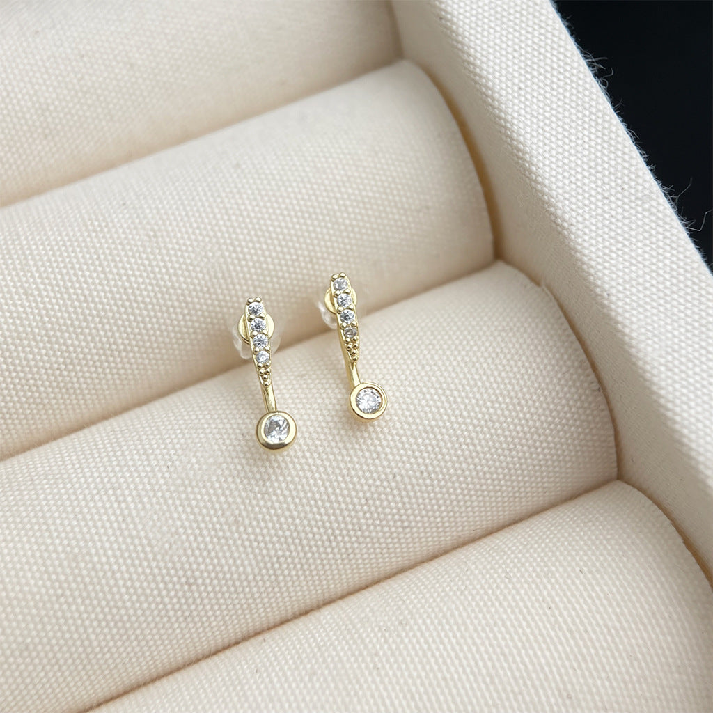 Gold earrings with small diamonds on a soft beige surface