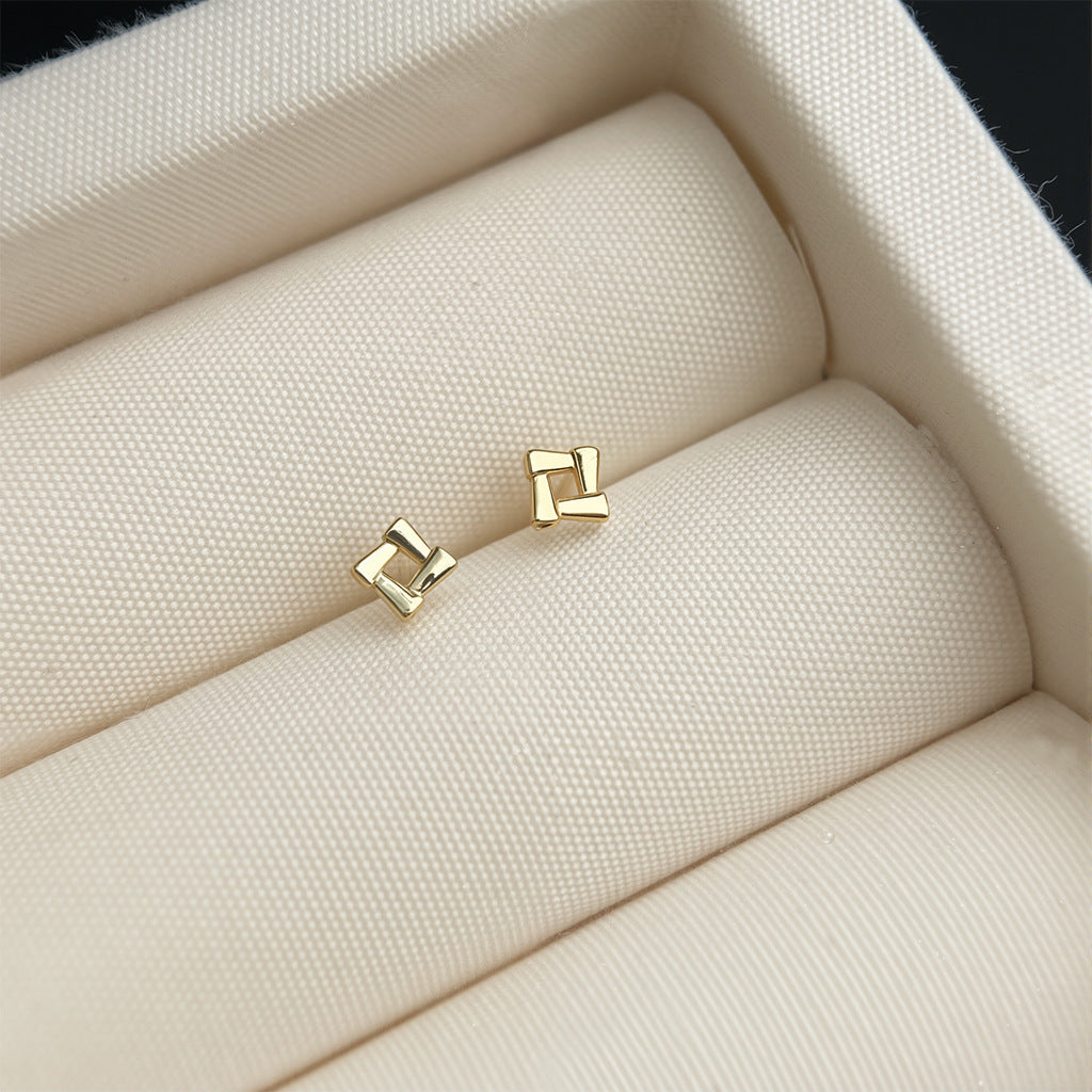 Gold square stud earrings on a beige fabric surface