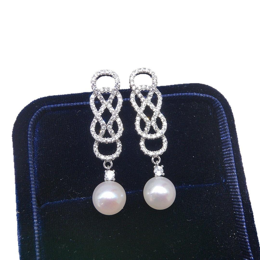 Pair of silver earrings with pearl drops on a black velvet stand.