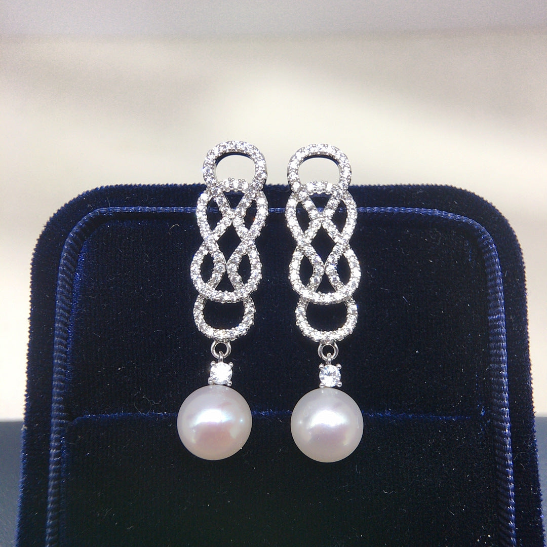 Pair of the pearl earrings with silver circular designs on a dark blue velvet stand.