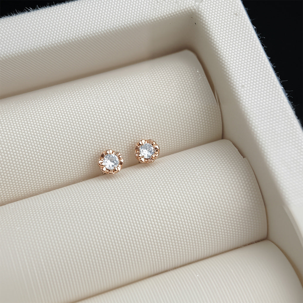 Rose gold earrings with clear gemstones on a textured beige surface