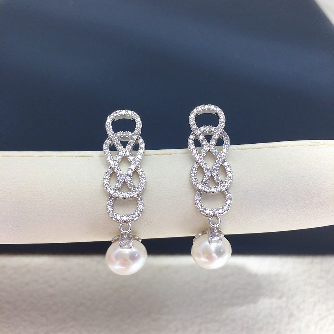 Silver earrings with intricate designs and pearl drops on a dark background