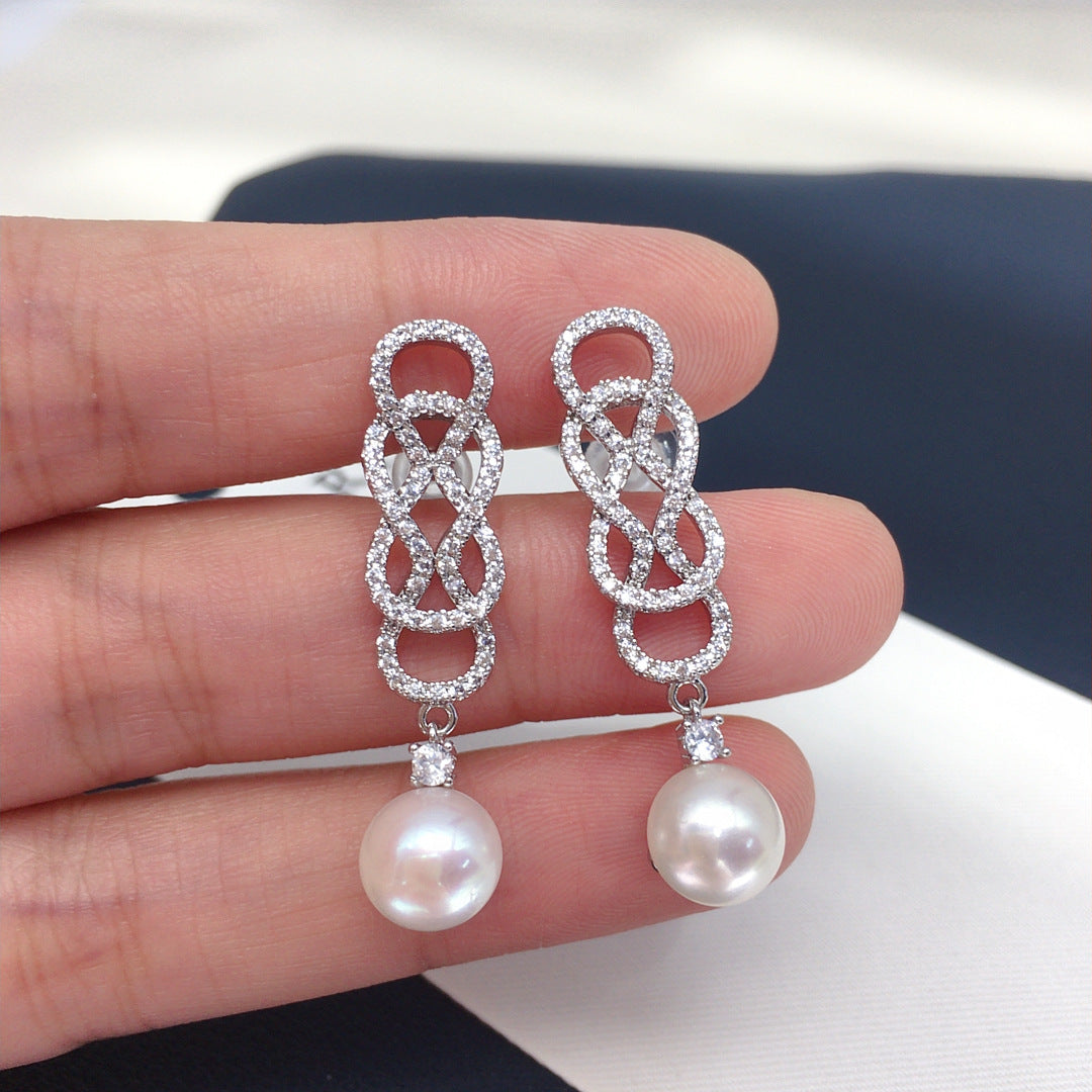 Silver earrings with pearl drops held between fingers against a neutral background