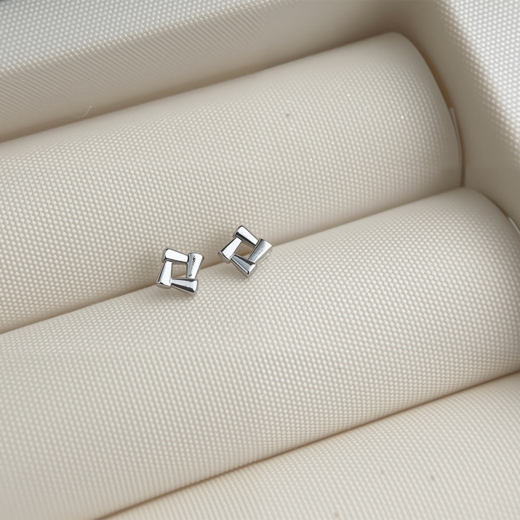 Silver geometric earrings on a textured beige surface