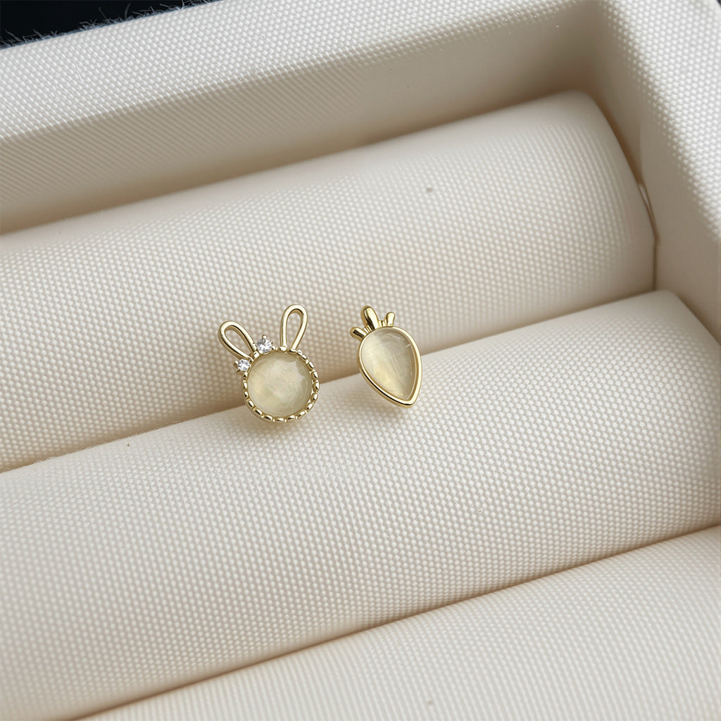 Two gold earrings on a textured beige surface